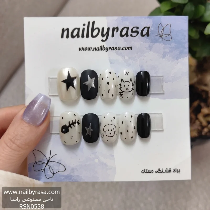 ناخن مصنوعی طرح کارتونی حیوانات و ستاره مشکی و شیری گرد راسا RSN0538، نمای نزدیک از ۱۰ عدد ناخن با طرح‌های متنوع شامل ستاره، خال‌خال، گربه، سگ و اسکلت ماهی به رنگ‌های سیاه و سفید صدفی روی بک‌گراند آبی.